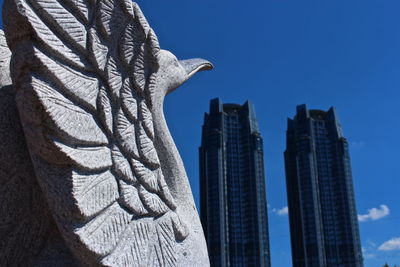 Low angle view of statue by towers against sky