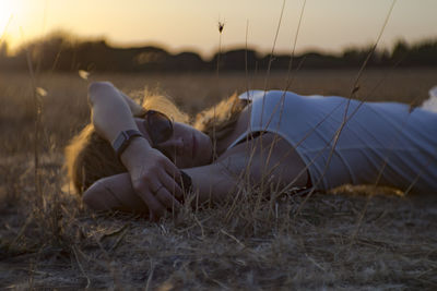 Young woman lying on grassy field during sunset