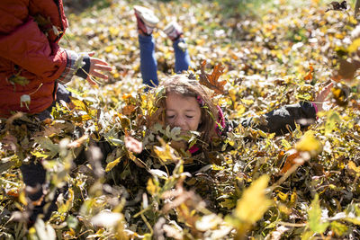 Siblings playing in leaves on field in yard during autumn