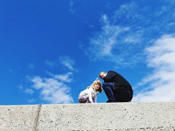 Low angle portrait of man with daughter against blue sky