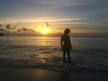 Rear view of silhouette man standing at beach during sunset