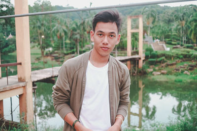 Portrait of young man standing against railing