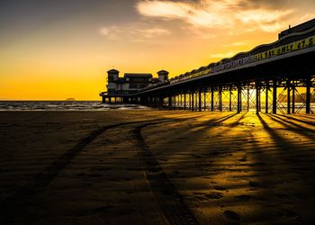 Stilt house in sea against sky during sunset