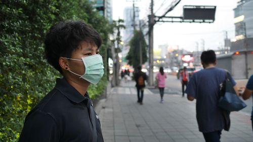 Man wearing pollution mask standing on sidewalk in city