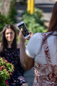 Woman taking picture of friend in the park with smartphone