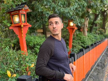 Handsome man looking away while standing by railing in park