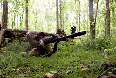 Woman lying down behind a rifle in a forest