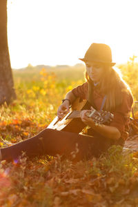 Young woman playing guitar on sunset in autumn field. candid silhouette woman in hat 