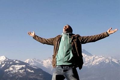 Young man with arms outstretched on mountain range in background