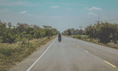 Rear view of person riding motorcycle on road against sky