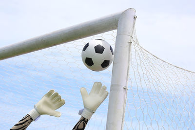 Cropped hand of goalie touching soccer ball against blue sky