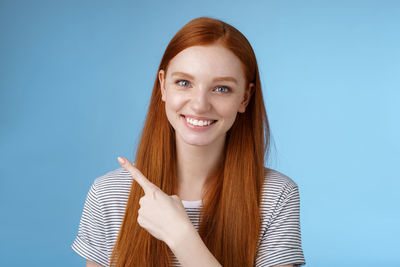 Smiling woman pointing against blue background