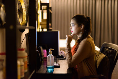 Side view of young woman using phone while sitting on table