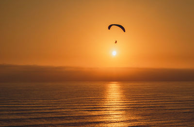 Parachute flying over sea against orange sky