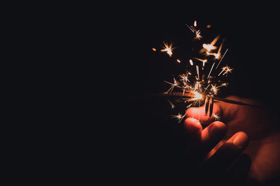 Cropped hand holding sparkler at night