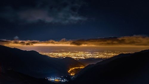 High angle view of silhouette mountains and illuminated cityscape at night