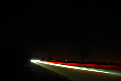 Light trails on road against clear sky at night