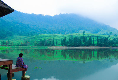 Rear view of boy looking at lake against sky