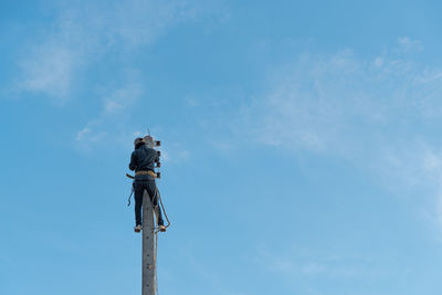 Low angle view of manual worker working on electricity pylon against sky