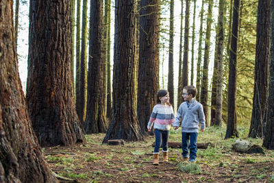 Boy and girl holding hands, walking through a forest.