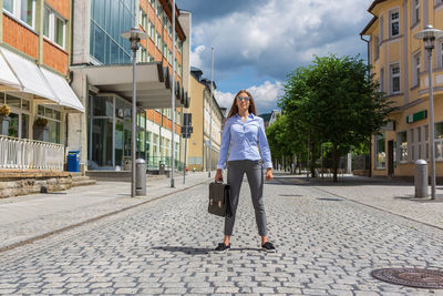 Portrait of woman standing on street amidst buildings in city