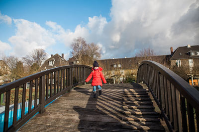 Rear view of woman walking on footbridge against sky