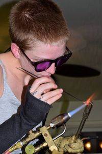 Young woman making glass with flaming torch in factory