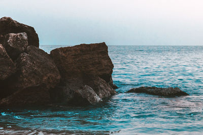 Rock formation in sea against clear sky