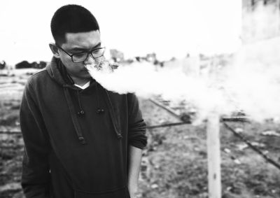 Man exhaling smoke on field against sky
