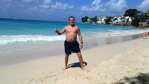 Shirtless man gesturing thumbs up sign at beach