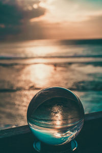 Close-up of glass against sea during sunset