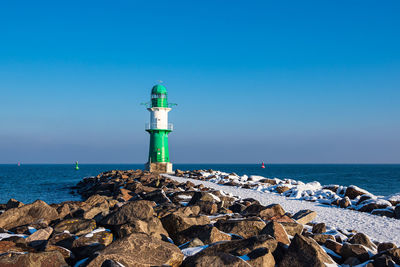 Lighthouse by sea against clear blue sky