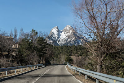 Road amidst trees and snowcapped mountains against sky