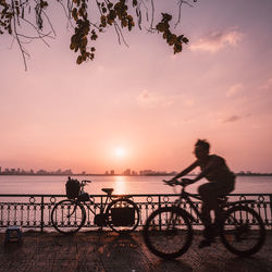 Silhouette man riding bicycle on river against sky during sunset