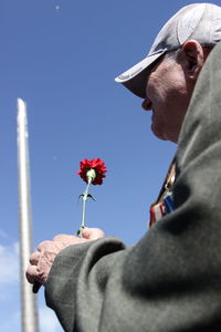 Close-up of man holding red flowering plant against sky