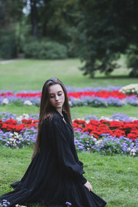 Side view of young woman sitting amidst flowering plants