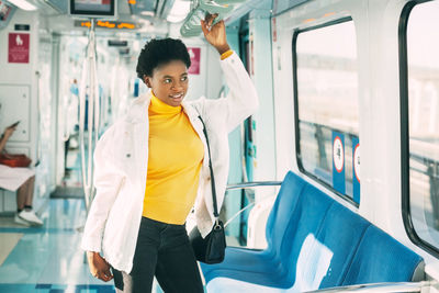 A smiling young african woman holds on to a handrail while standing on a subway 