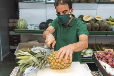 A man cutting a pineapple in his own fruit shop.