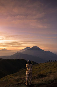 Rear view of man standing on mountain during sunset