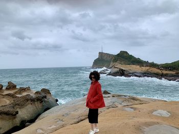 Portrait of woman sanding on rock formation against sky