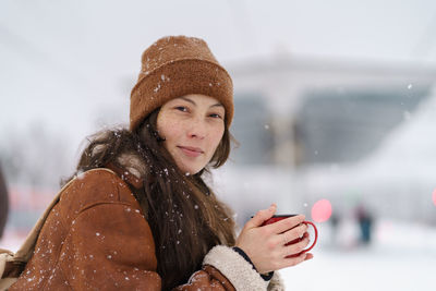 Young asian girl traveler hold cup of hot tea wait for train arrival on outdoor station travelling