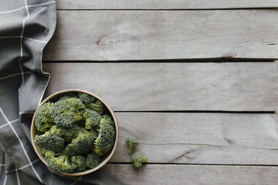 Green fresh broccoli in bowl on wooden background, gray towel. healthy eating concept