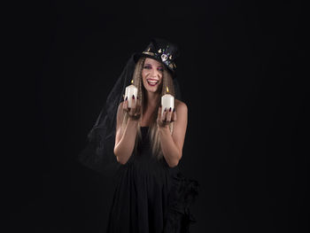 Portrait of young woman standing against black background