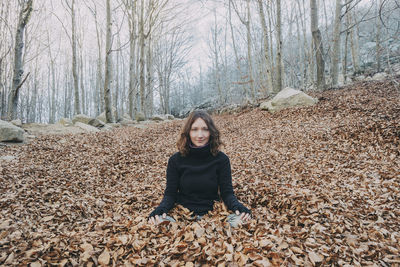 Portrait of smiling young woman on dry leaves in forest