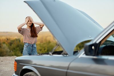 Rear view of young woman standing against car