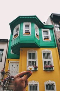 Person holding umbrella on building against sky