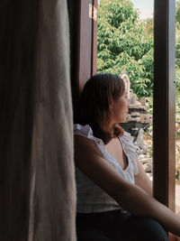 Side view of woman looking through window at home