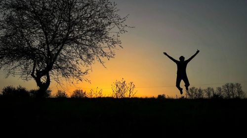 Silhouette of person jumping on field against sky during sunset