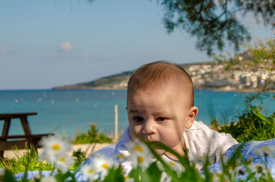 Cute baby boy on plants against sea