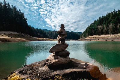 Statue on rock by lake against sky